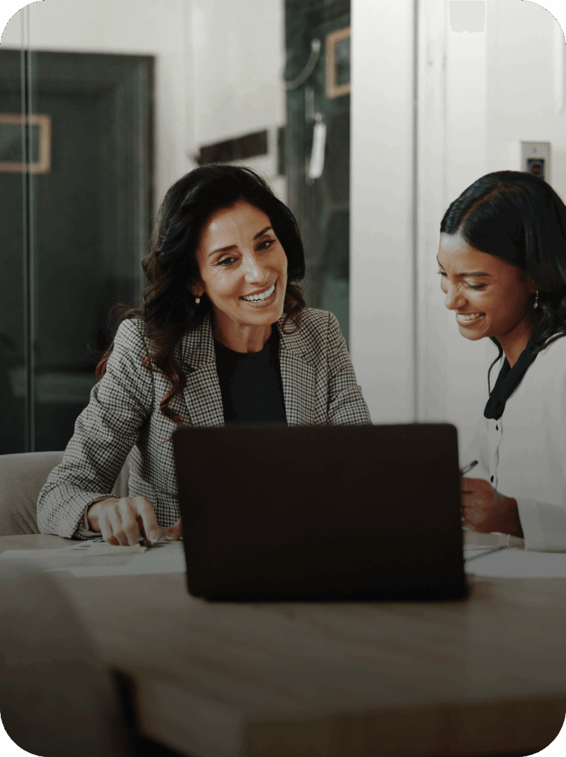 Two women smiling while working on laptop.
