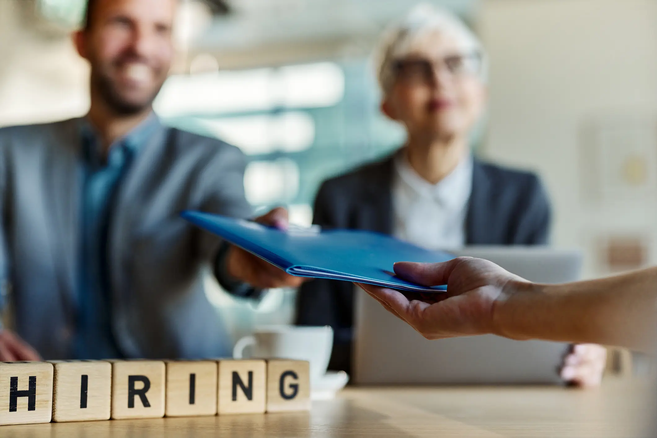 Close up of wooden blocks with single word 'hiring' and unrecognizable candidate giving resume on a job interview.
